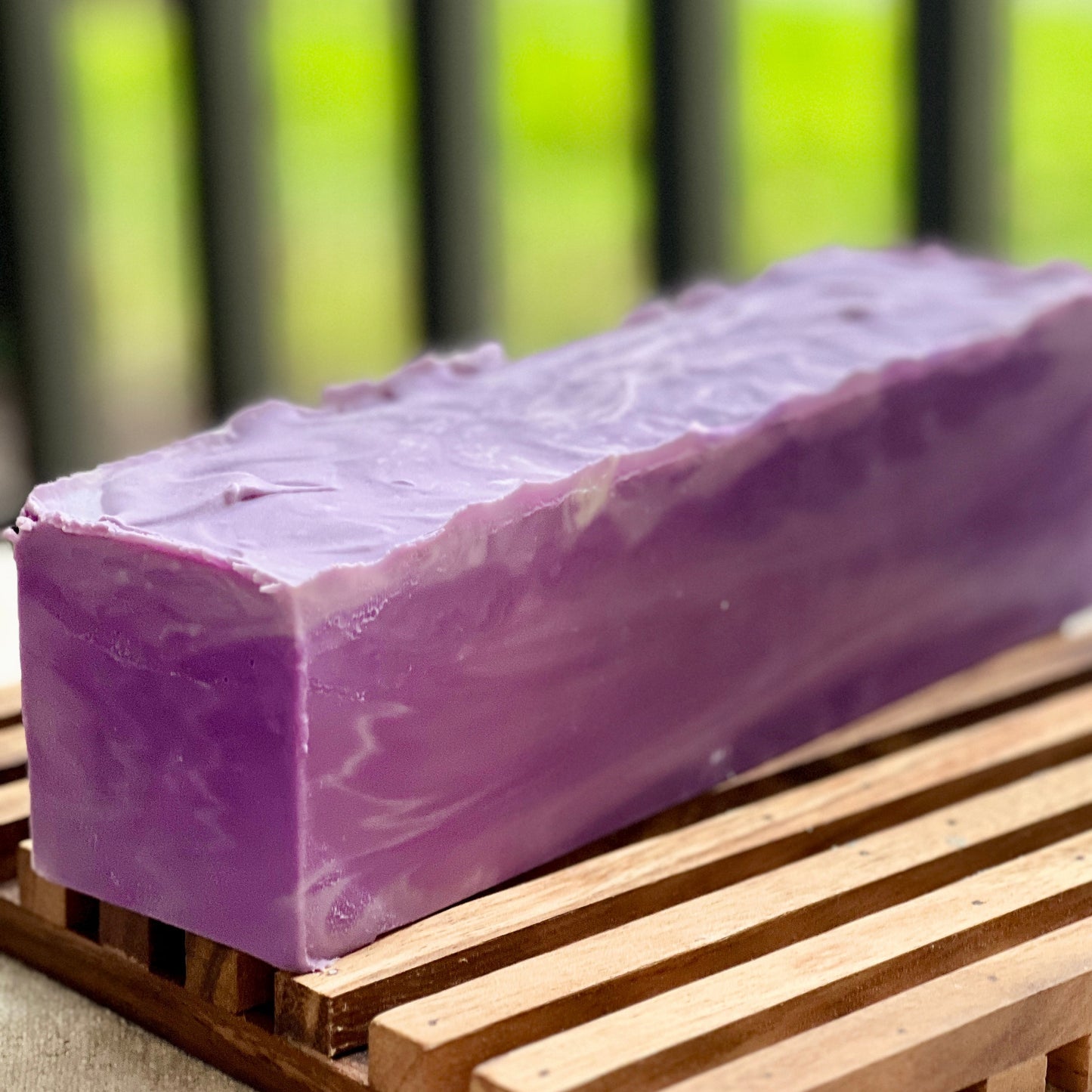 Purple soap bar on a wooden surface with a blurred green background